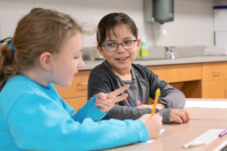 Students working together in the classroom, counting on fingers and smiling